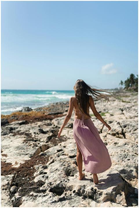 A woman walks along the rocky shore of Tulum, Mexi