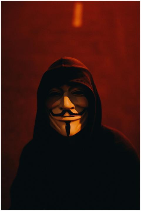 A person wearing a Guy Fawkes mask and hood in a d
