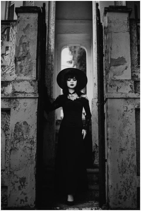 A woman in a vintage black dress and hat stands in