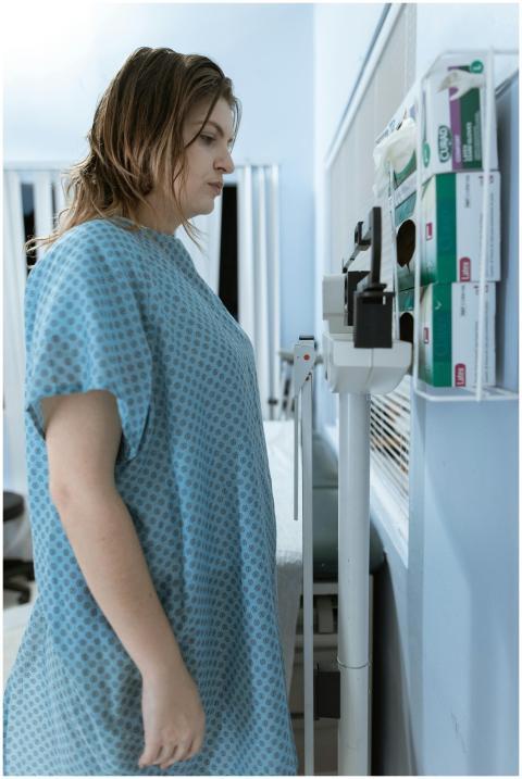 A woman in a hospital gown using a scale in a medi