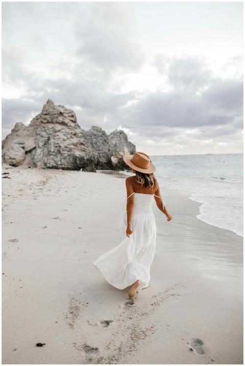 A woman in a white dress and straw hat strolls alo