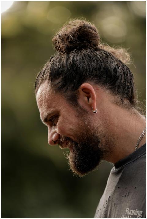 Close-up profile of a bearded man with a bun smili