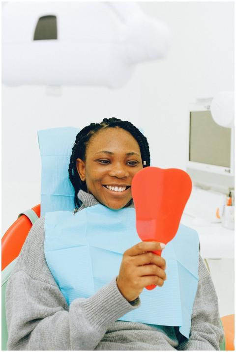 Smiling woman in a dental clinic holding a mirror,