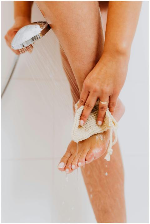 A woman washing her foot under a showerhead in a c