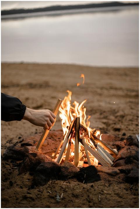 A close-up of a bonfire being tended to on a sandy