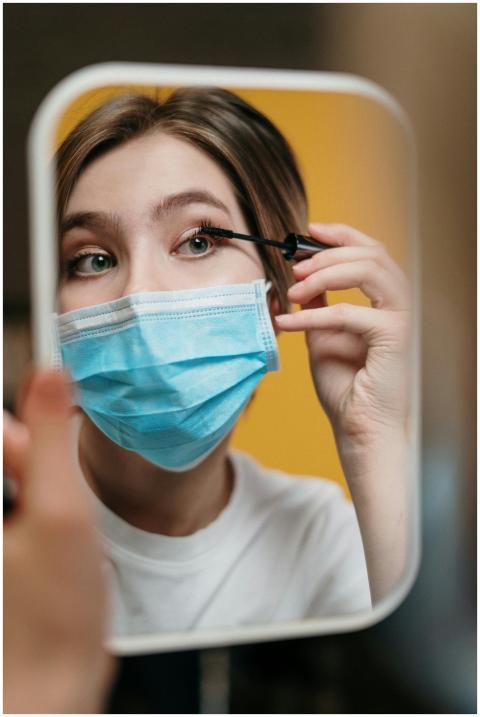 Woman in a face mask applying mascara in front of