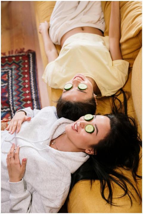 Two women relaxing with cucumber eye masks on a so