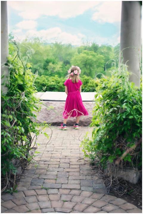 A girl in a bright pink dress stands in a lush gar