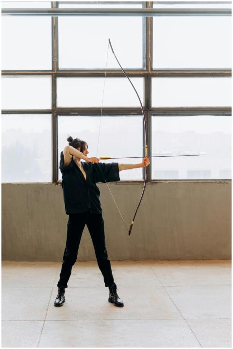 Woman practicing archery indoors, showcasing focus