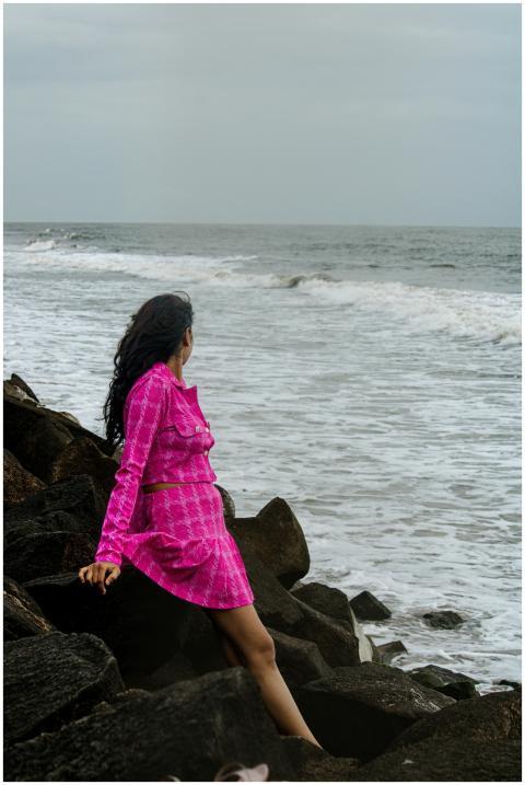 Woman in a pink dress sitting on rocks by the ocea