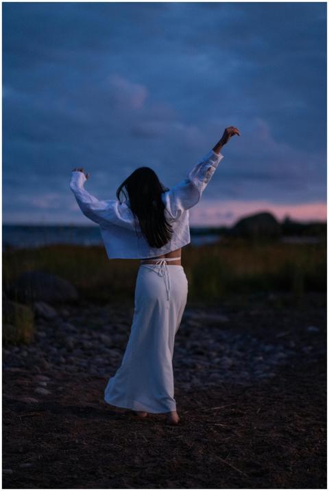 A woman dances freely by the seaside at twilight,