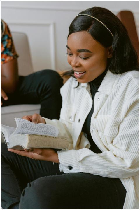 Smiling young woman engaged in reading a bible ind