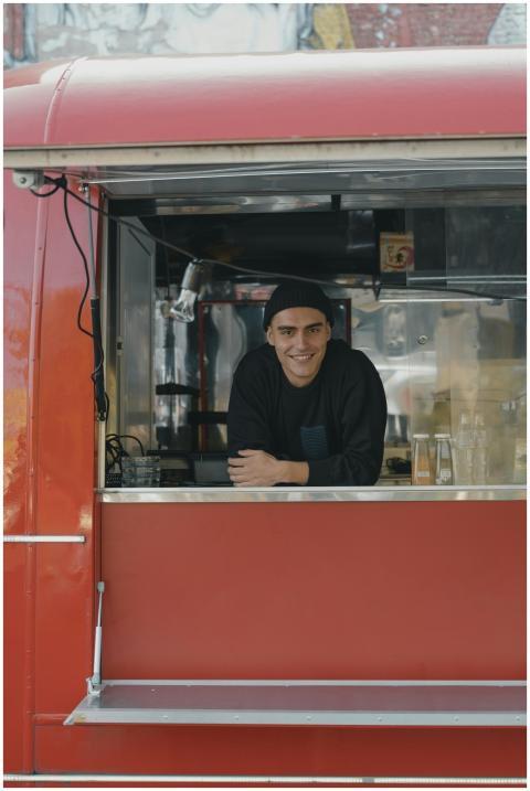 Smiling vendor in a red food truck serving outdoor