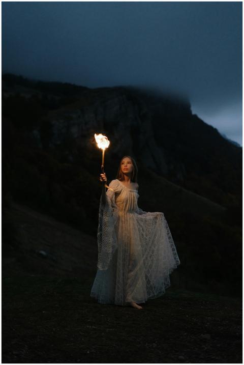 A woman in a white gown holds a lantern, illuminat