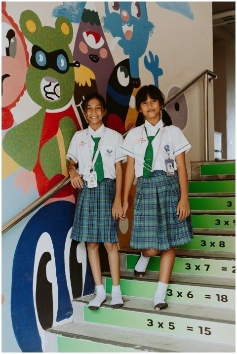 Two schoolgirls in uniform pose on vibrant stairs
