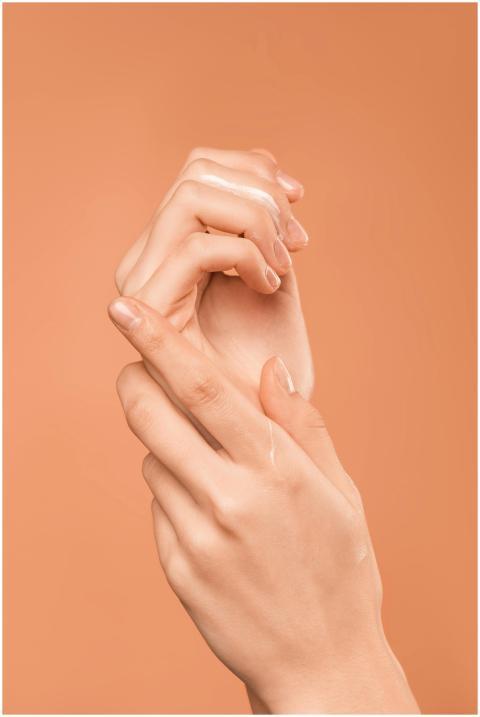 Close-up of hands with oil on peach background, em