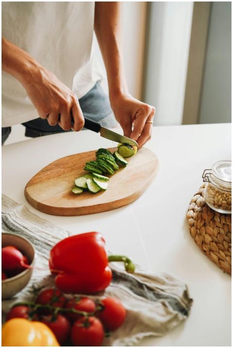 Close-up of hands slicing cucumber on a cutting bo