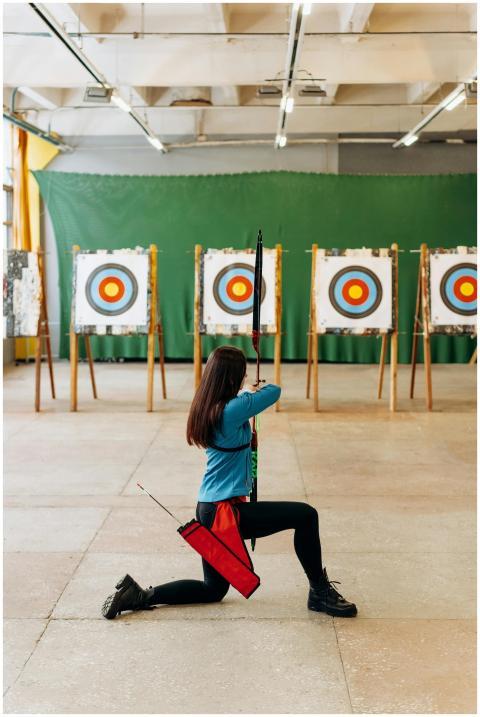 Woman practicing archery indoors, aiming at multip