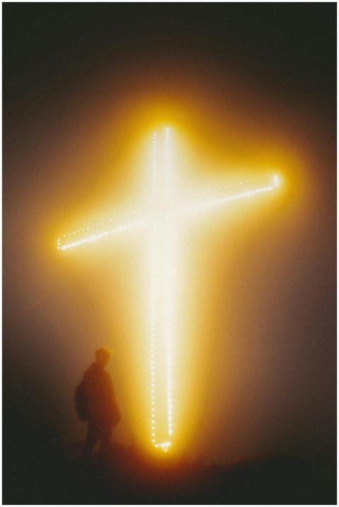 Silhouette of a man by a glowing cross at night in