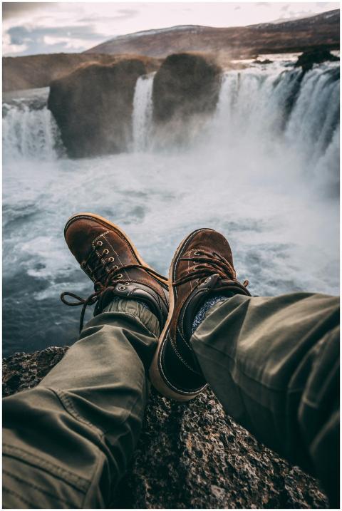 Person in hiking boots sitting at cliff's edge, ov