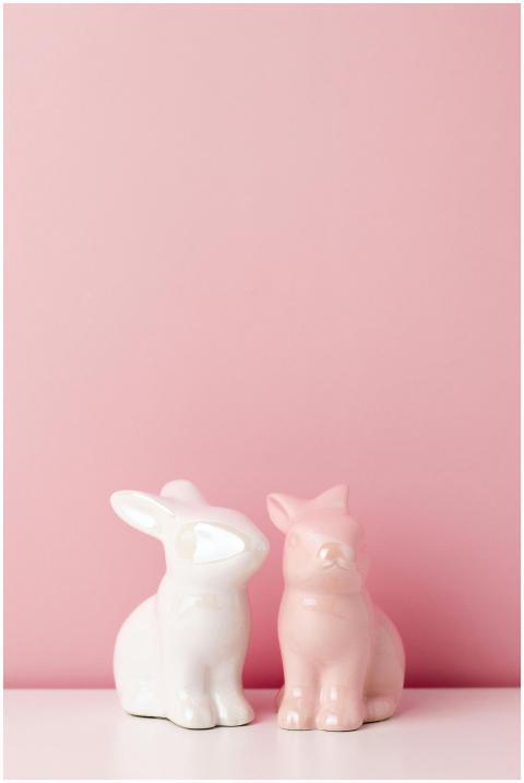 Two pastel ceramic bunny figurines against a pink