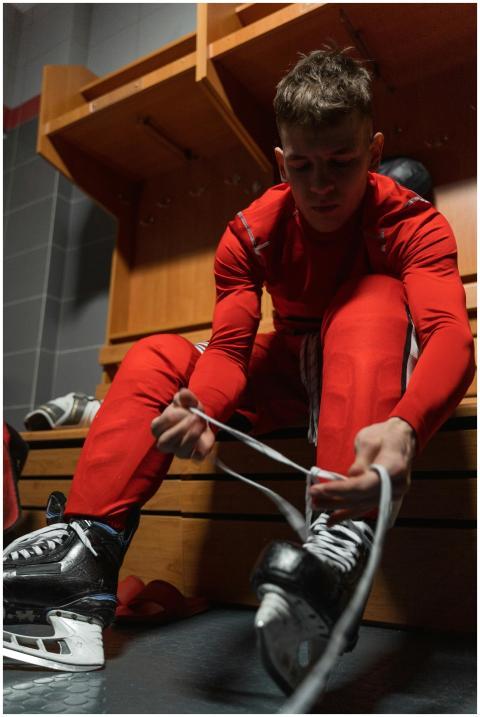 A young man in a locker room ties his ice skates b