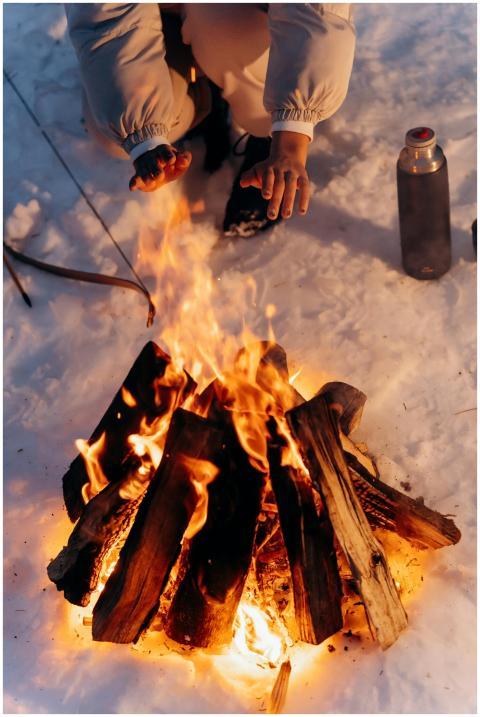 A person warms their hands near a campfire in a sn