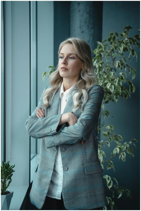 A poised female executive standing by a window, em