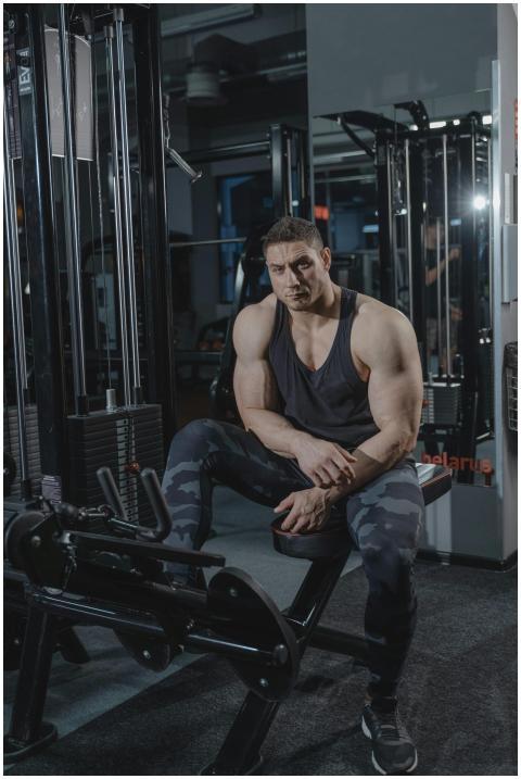 A muscular man in workout attire sitting on gym eq