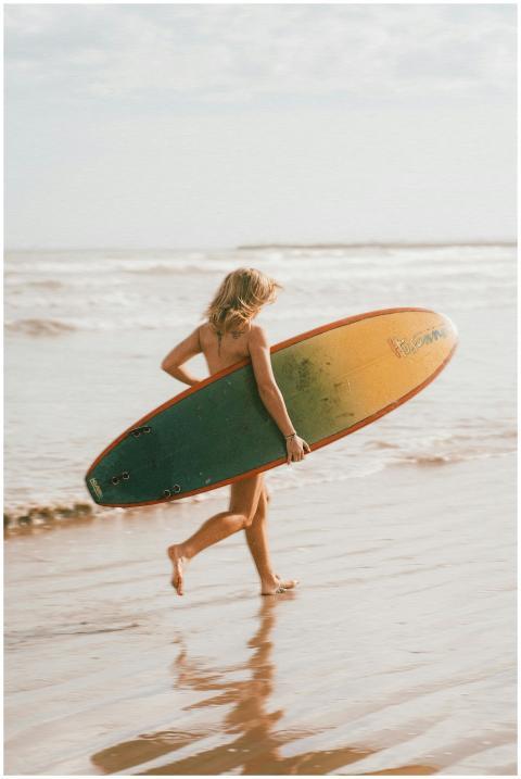 A young woman carries a surfboard on a sunny beach