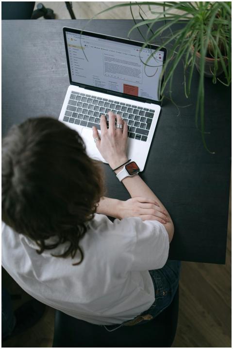 A person sits at a black table, using a laptop for