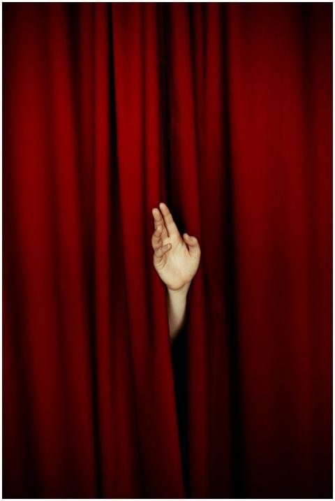 A hand appears between rich red velvet curtains, e