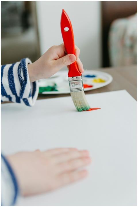 Close-up of a child painting with a red brush on a