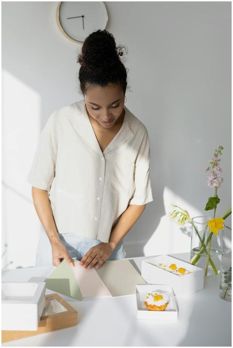 A young woman packages cupcakes in a sunlit modern