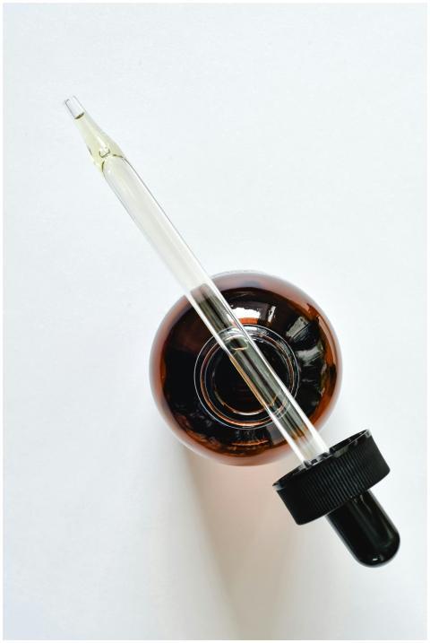 A glass pipette and amber bottle on a white surfac