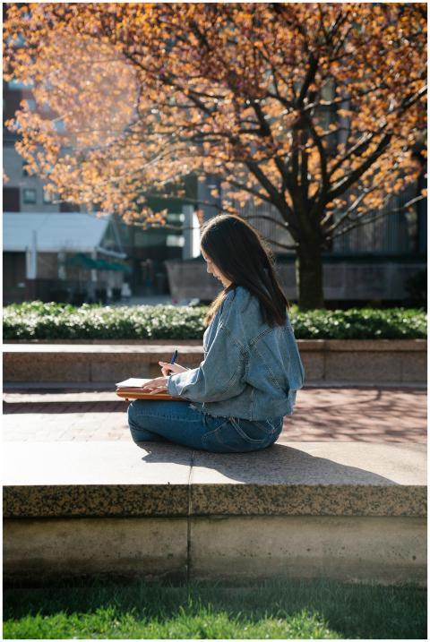 A young woman in casual attire writes in a noteboo
