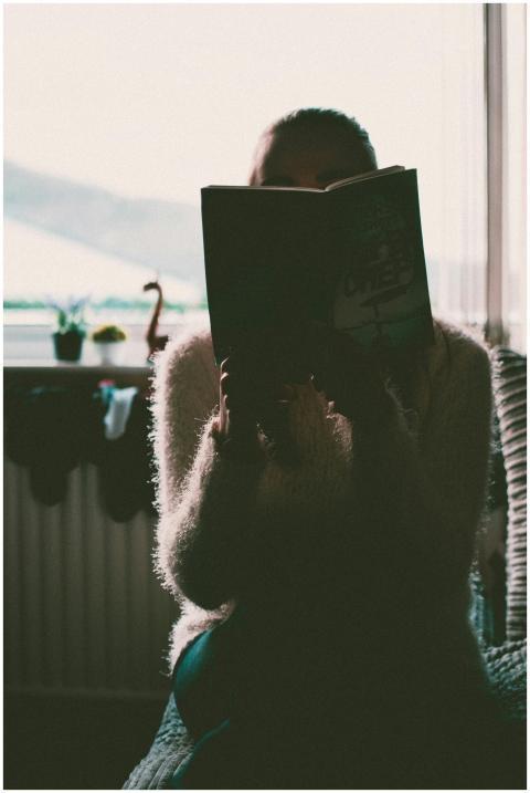 A woman in silhouette reading a book indoors by a