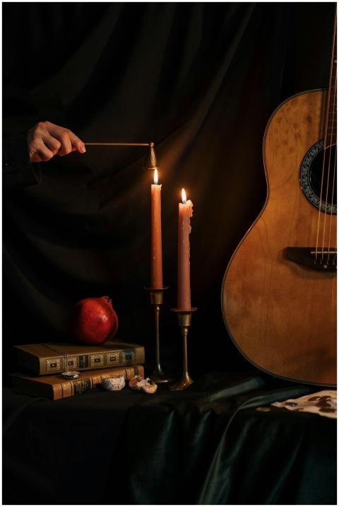 A dark still life scene with candles, a guitar, bo