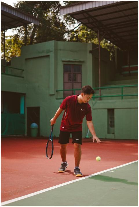 A young male tennis player bouncing a ball on an o