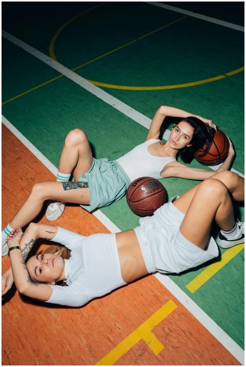 Two women lying on a basketball court, posing conf