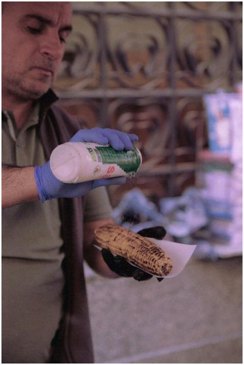 Street vendor grilling and seasoning corn at a mar