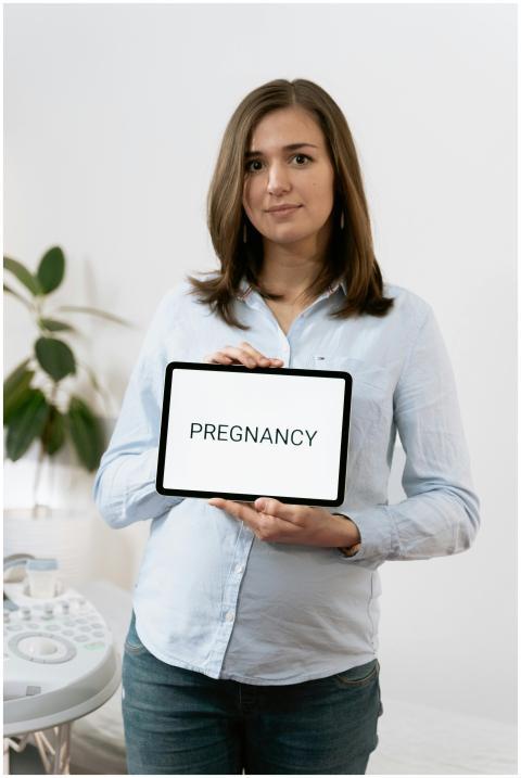 A pregnant woman stands in a medical clinic, holdi