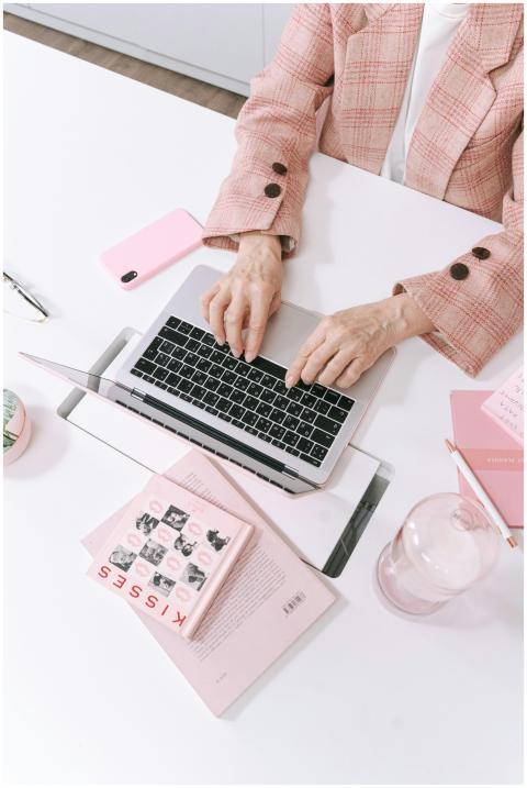 An adult typing on a laptop in a stylish pink-them