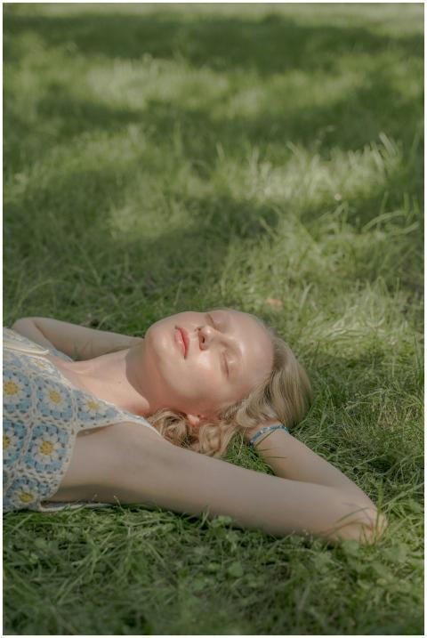 A young woman with eyes closed, laying on grass, e