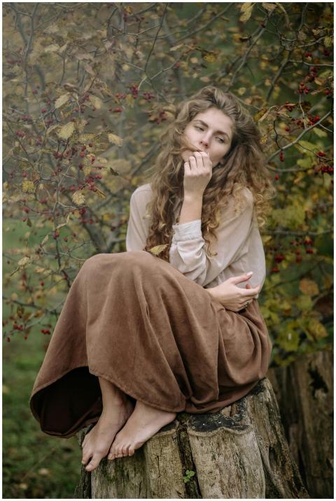 Thoughtful woman sitting on a tree stump in an aut