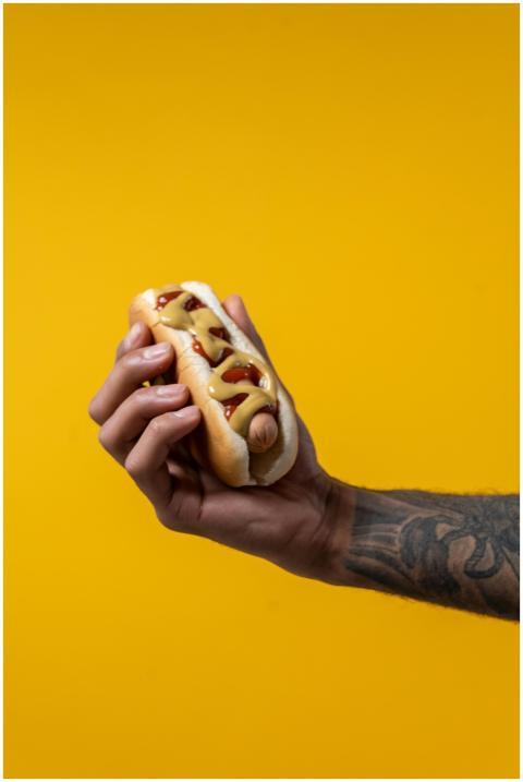 A person holding a mustard and ketchup hot dog aga