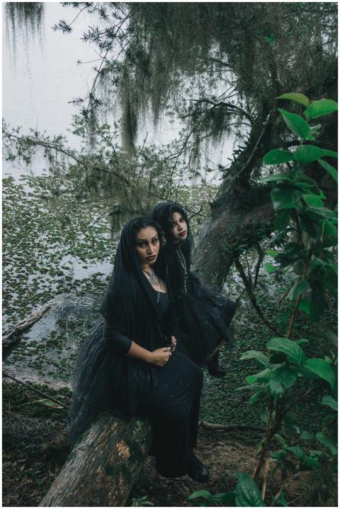 Two women in gothic attire sit on a log in a mysti
