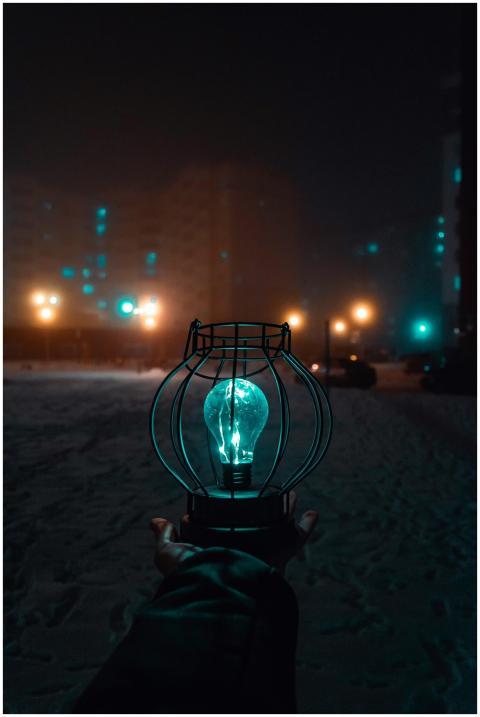 A hand holds a glowing bulb in a snowy city street