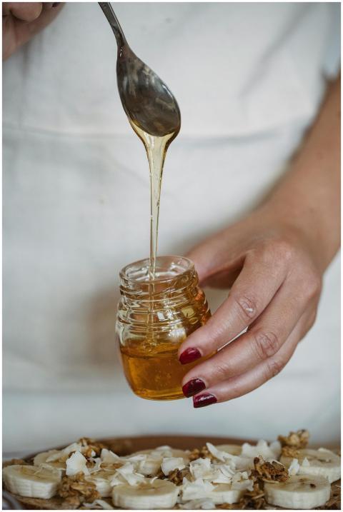 A hand drizzling honey from a jar over fresh banan