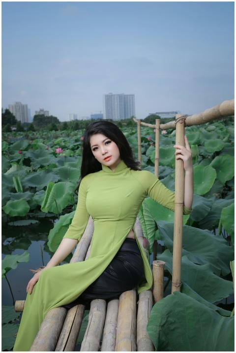 Asian woman in green ao dai posing by lotus pond,